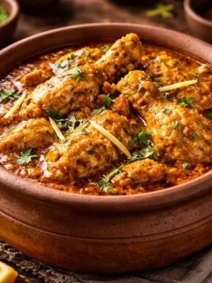 A clay handi of creamy chicken curry garnished with ginger, green chillies and coriander, served with naan