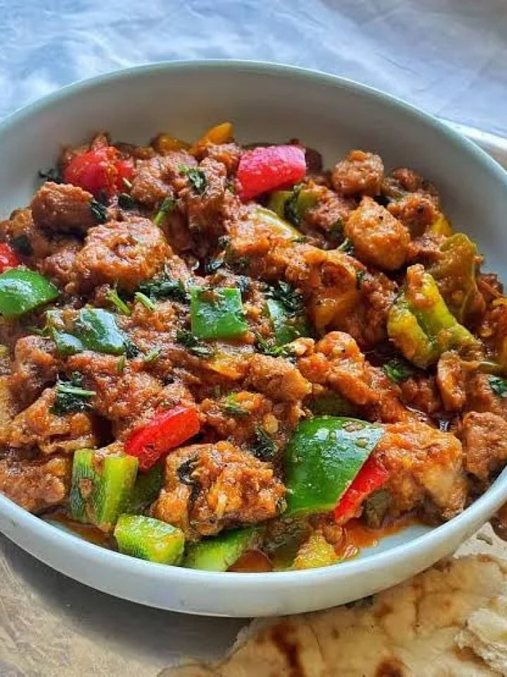 A pan of chicken jalfrezi with red and green peppers, onion wedges and fresh ginger in a thick tomato masala