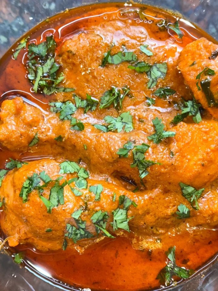A pot of creamy golden chicken korma garnished with coriander and green chillies, served with naan and basmati rice.