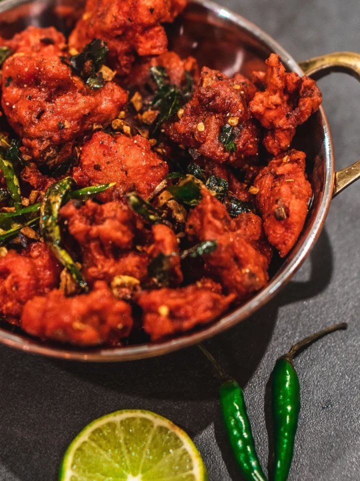 A plate of golden fried chicken pakoras with mint chutney, lemon wedges and onion rings