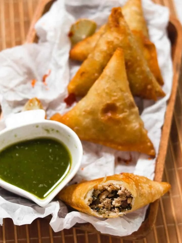 Golden fried chicken samosas on a plate with one split open showing spiced chicken mince, served with chutneys