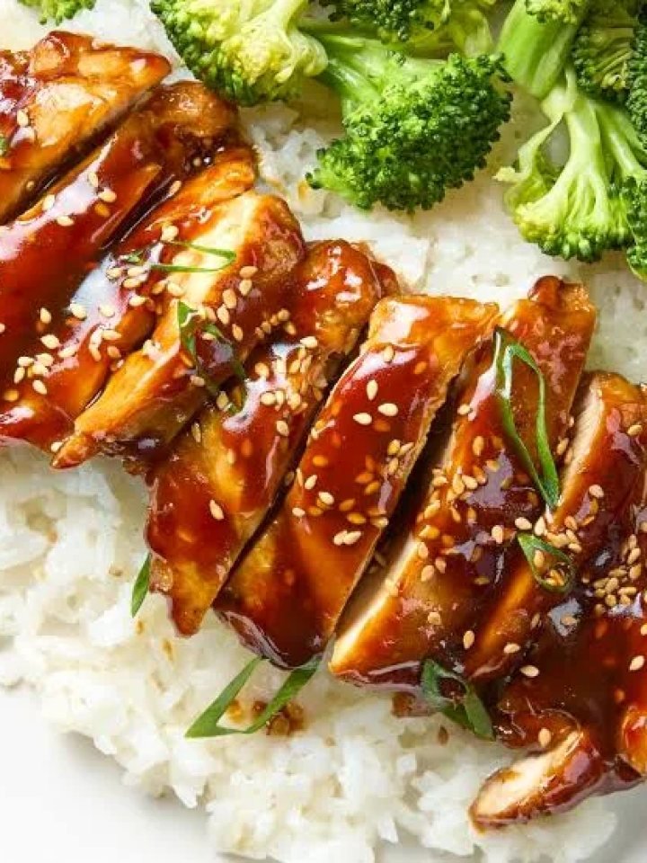 Sliced chicken teriyaki with glossy glaze, rice and broccoli on a white plate