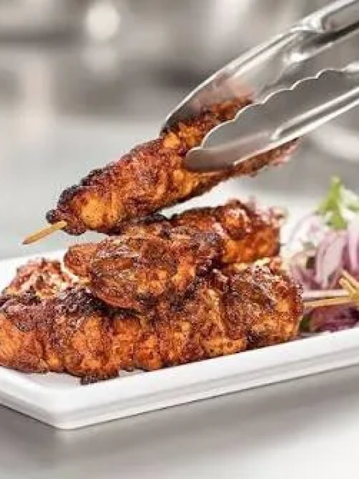 Skewers of charred, red-orange chicken tikka boti served with onions, lemon wedges, chutney and naan