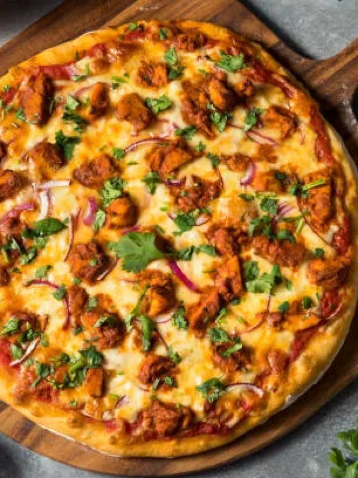 Chicken tikka pizza topped with mozzarella, peppers, onion and coriander on a wooden board