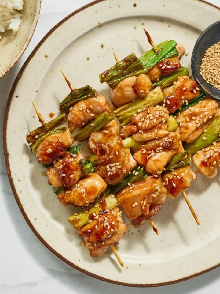 Glazed chicken yakitori skewers with spring onion on a dark plate with lemon wedges and dipping sauce