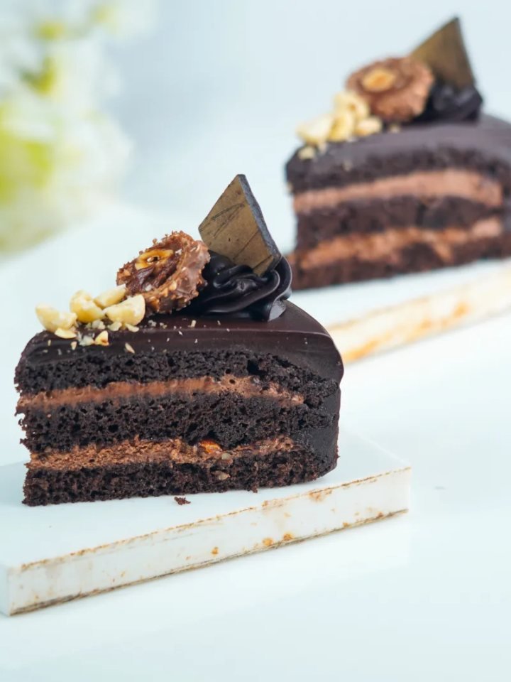 Sliced two-layer chocolate cake with glossy chocolate ganache on a white cake stand