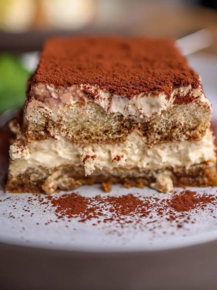 A slice of coffee tiramisu with visible layers of ladyfingers and mascarpone cream, dusted with cocoa powder