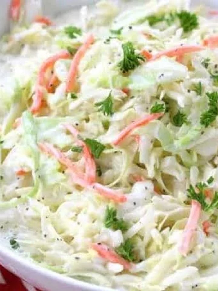 A white bowl of creamy coleslaw with shredded cabbage, carrot and fresh parsley