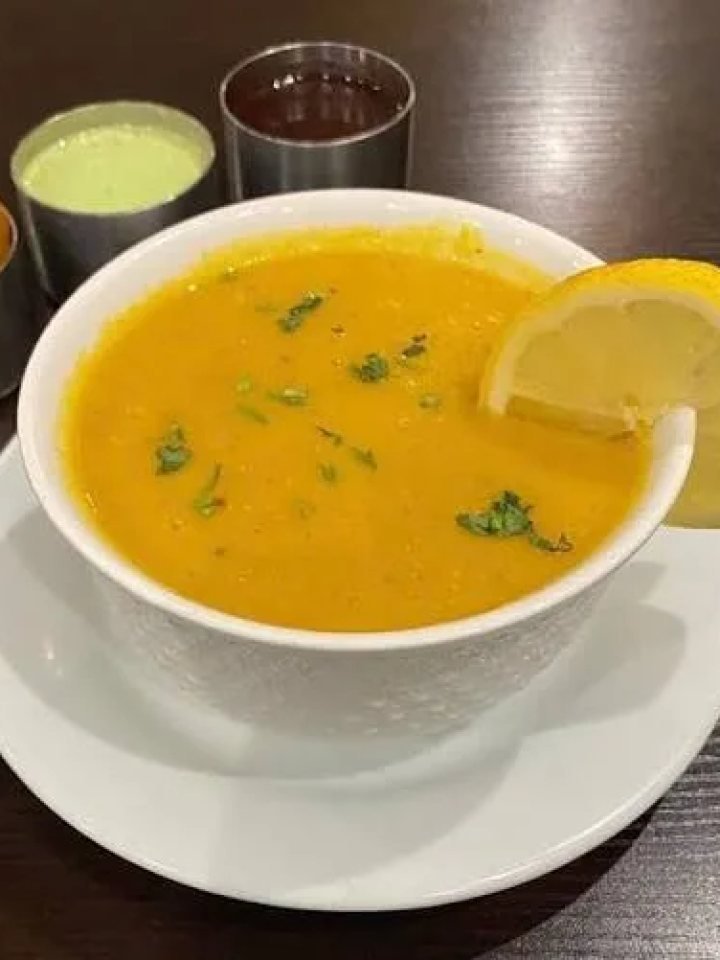 Bowl of smooth golden lentil soup topped with cumin and garlic tarka, coriander and a lemon wedge