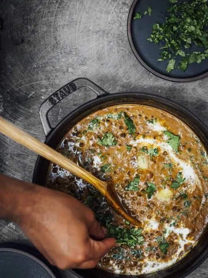A bowl of creamy dal makhani topped with cream and butter, served with naan and lemon wedges
