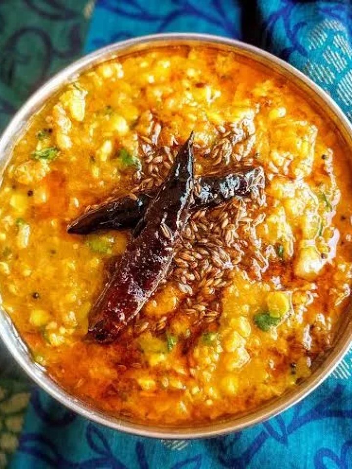 A bowl of golden dal tadka topped with garlic, red chilli and coriander, served with rice and roti