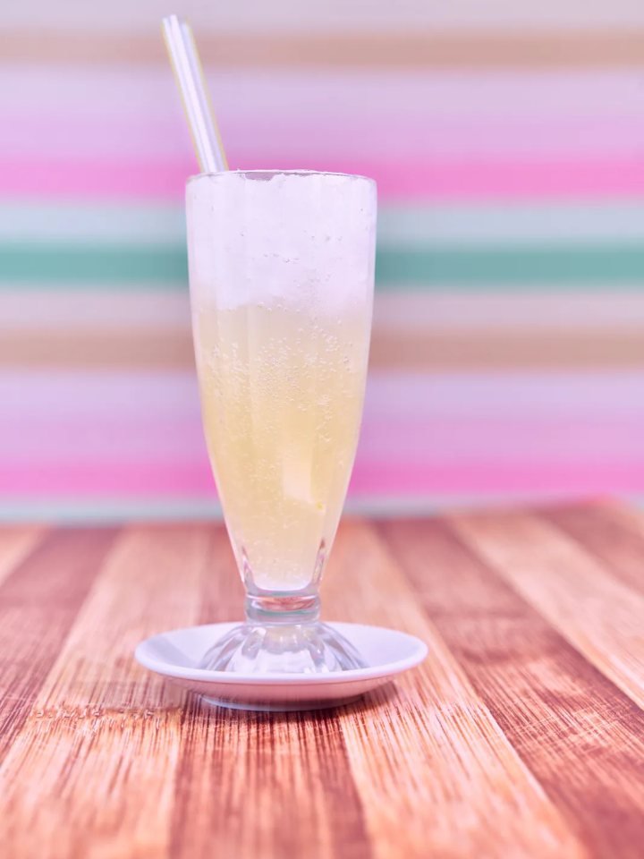 Two tall glasses of pale pink Doodh Soda with ice and a fizzy foam top, garnished with dried rose petals