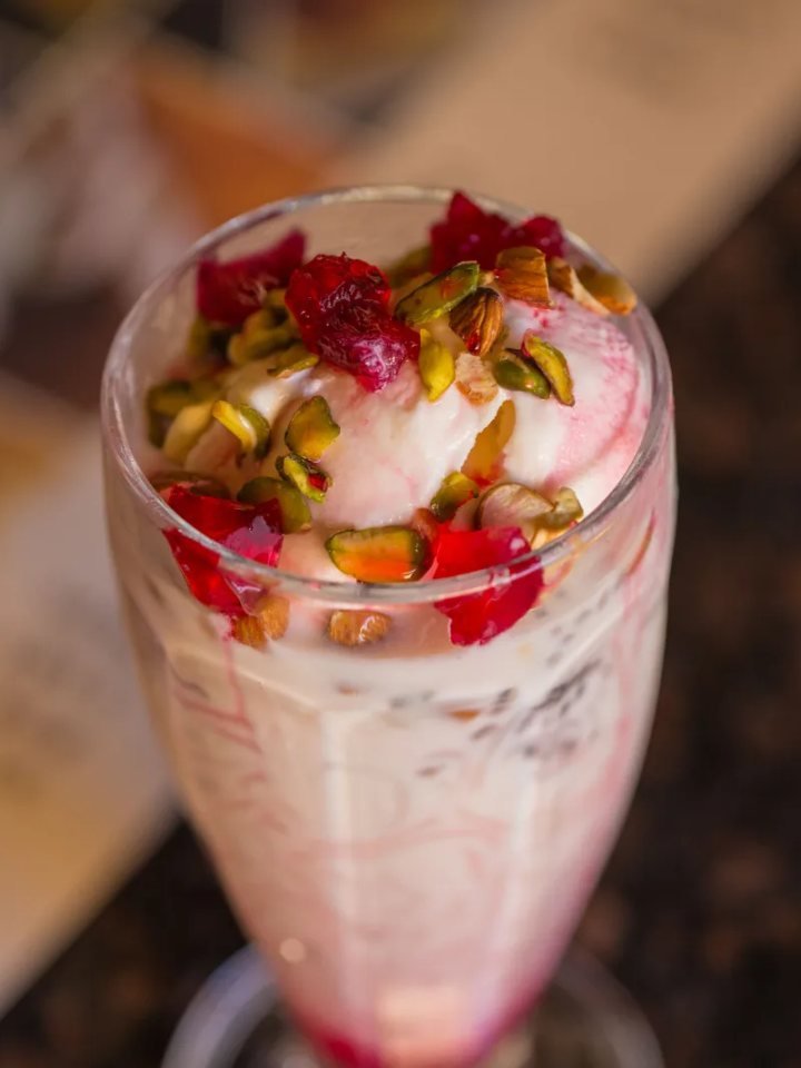 Tall glasses of pink falooda layered with vermicelli, basil seeds and jelly, topped with ice cream and nuts