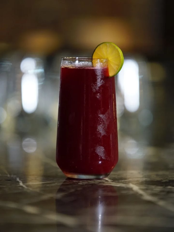 Glasses of deep purple falsa sharbat with ice and mint beside a bowl of fresh falsa berries