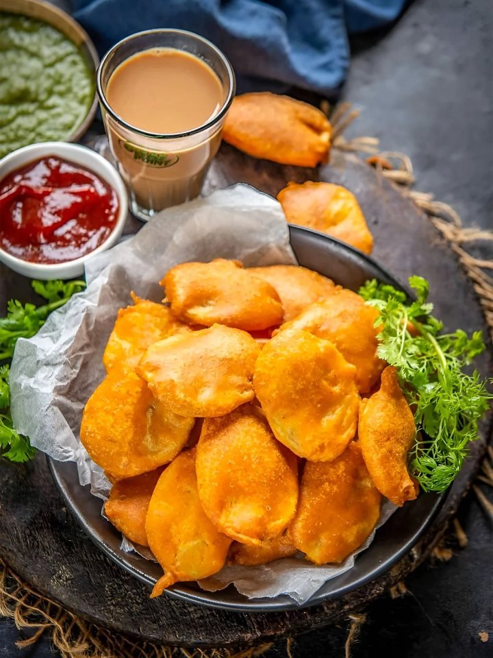 A plate of golden crispy fish pakoras with mint chutney, tamarind chutney and lemon wedges