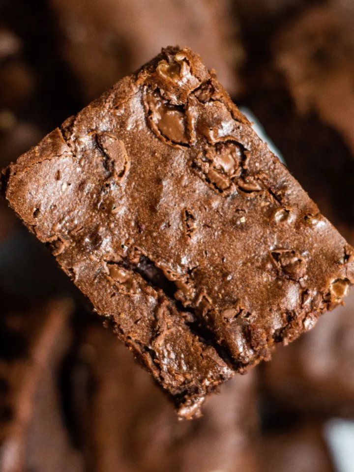 Squares of fudgy chocolate brownies with crackly tops stacked on baking paper, one broken open to show a moist centre