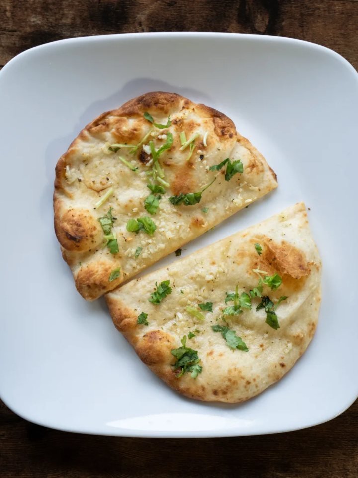 Stack of golden garlic naan brushed with garlic butter and coriander on a wooden board