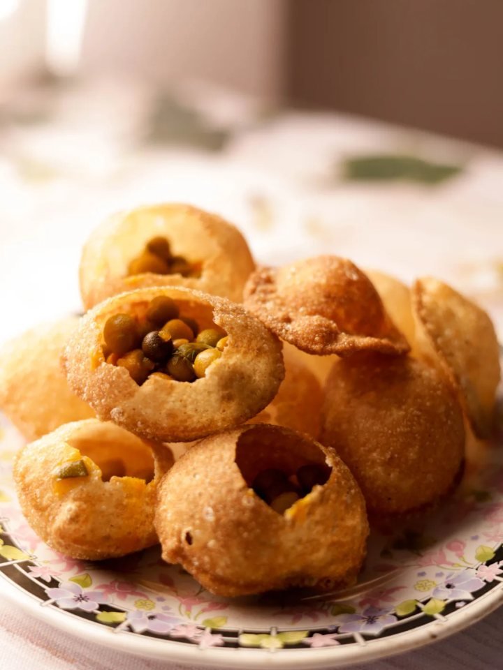 Golden gol gappay shells on a platter with a jug of green mint pani and bowls of chickpea filling