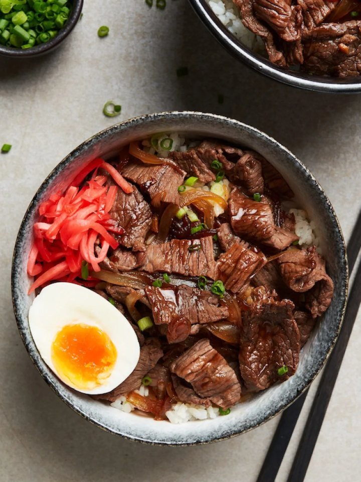 Bowl of gyudon with simmered beef and onions over white rice, topped with spring onions and sesame seeds