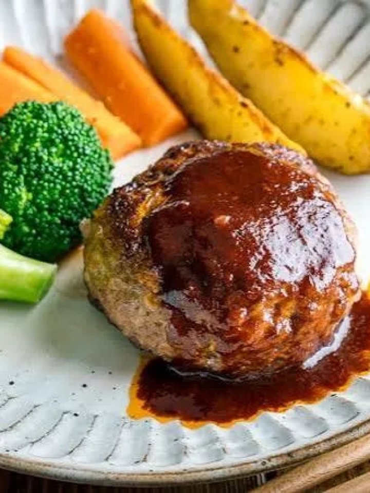 Hambagu steak patties in glossy brown sauce with mushrooms, rice and vegetables on a white plate