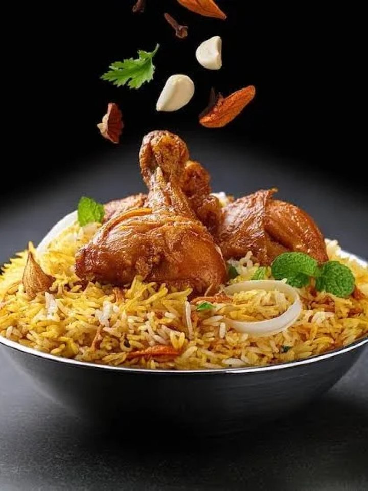 Open pot of Hyderabadi chicken biryani with saffron rice, chicken pieces, fried onions and fresh herbs
