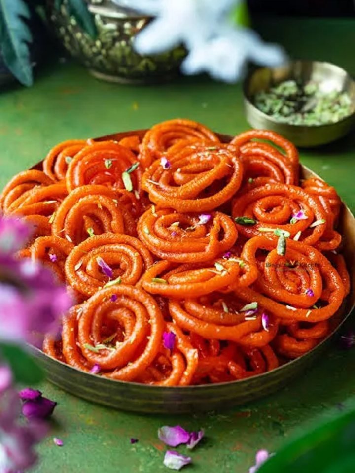 A plate of golden-orange jalebi spirals glistening with saffron syrup and topped with chopped pistachios