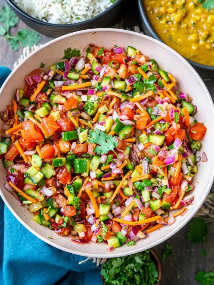 Bowl of diced cucumber, tomato and red onion salad with coriander, mint and pomegranate seeds beside lemon halves