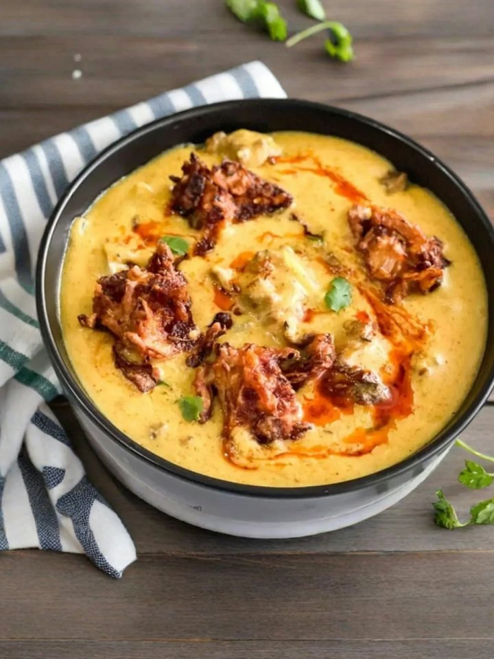 A bowl of golden yellow kadhi with soft pakoras, red chilli tarka and fresh coriander, served with white rice