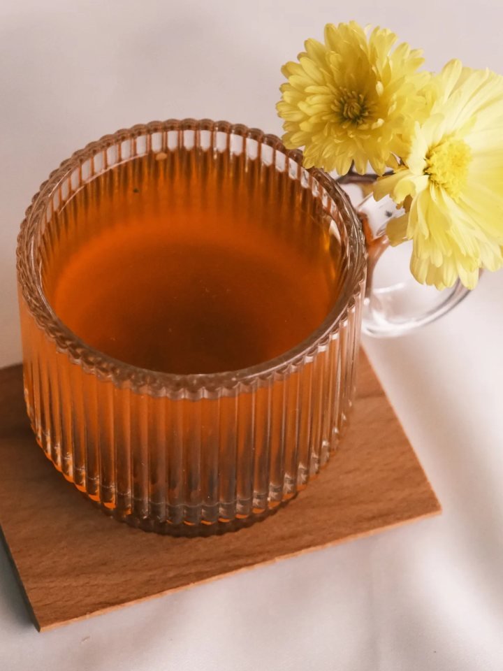 Glass cups of golden Kashmiri kahwa tea topped with sliced almonds, beside a teapot, cinnamon sticks and cardamom pods