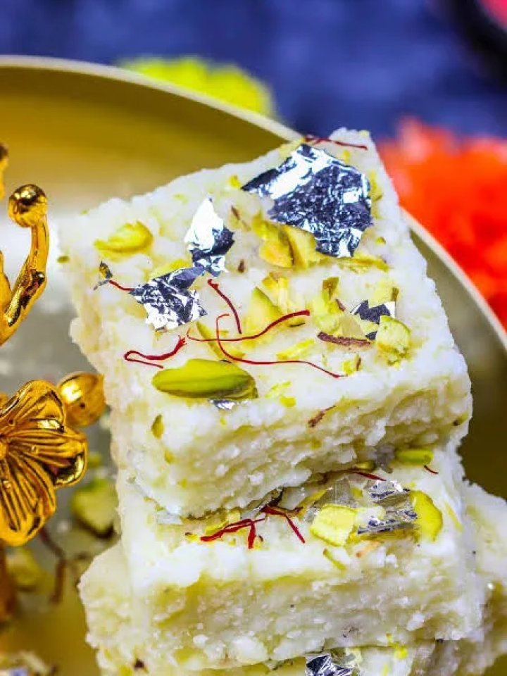 Square pieces of creamy kalakand topped with sliced pistachios on a white plate