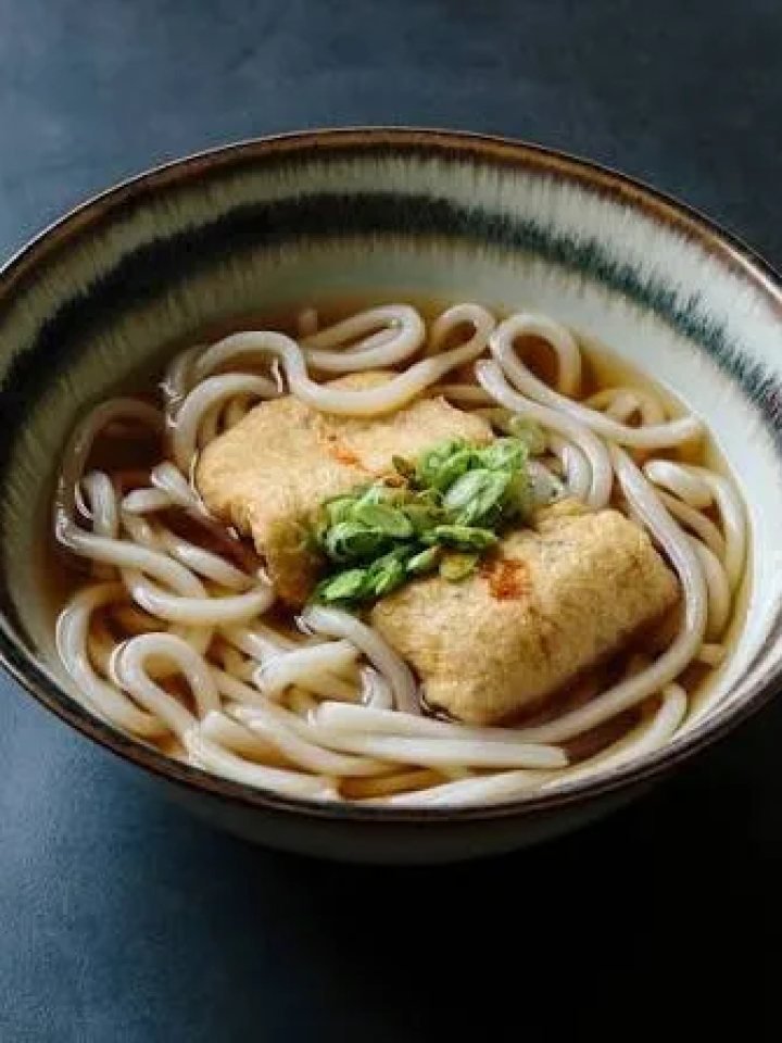 Bowl of kitsune udon with sweet simmered tofu pouches, spring onions and carrot in golden broth