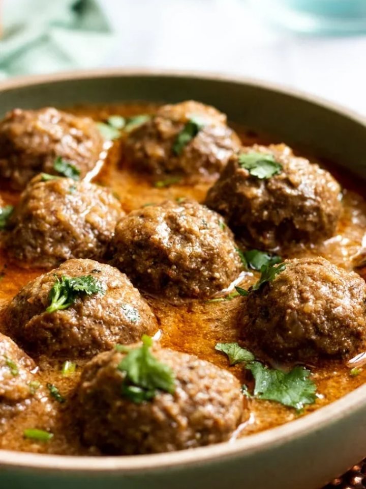 A pot of Pakistani kofta curry with beef meatballs in red tomato gravy, garnished with coriander, ginger and green chillies