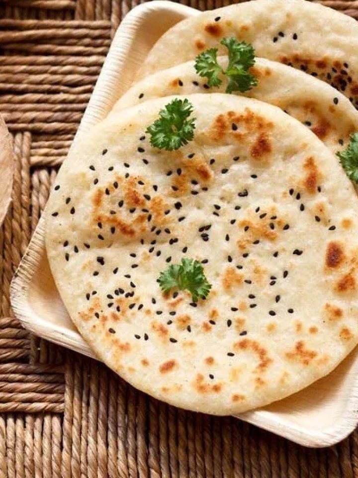 Stack of freshly baked kulcha breads with sesame and nigella seeds on a wooden board