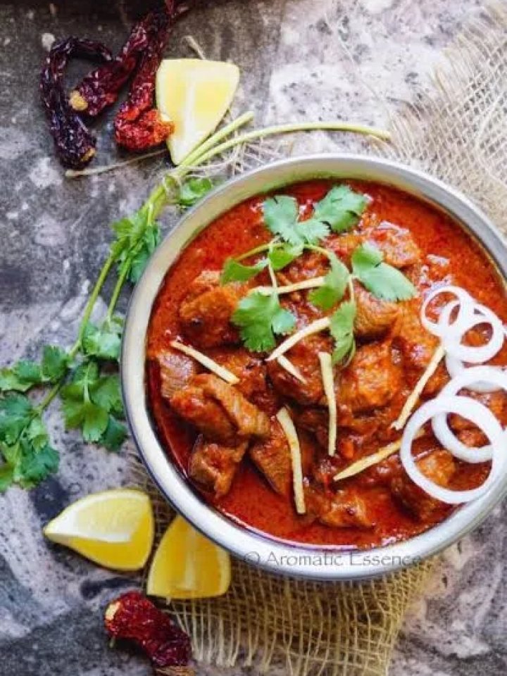 Brass pot of deep red Laal Maas mutton curry garnished with coriander, served with bajra roti and onions