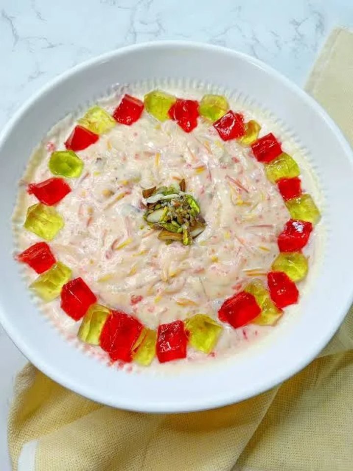 Glass bowl of Lab-e-Shireen with custard, red jelly cubes, mixed fruit, pistachios and pomegranate seeds