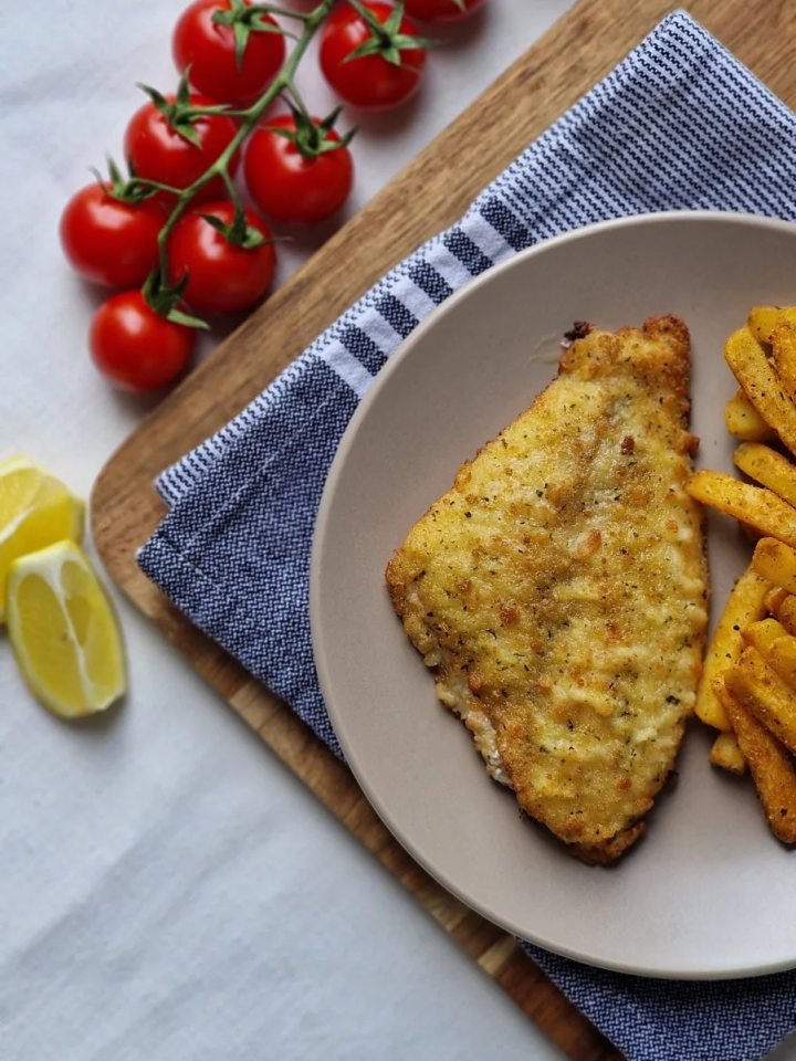 Golden crispy Lahori fried fish pieces on a platter with lemon wedges, onion rings and green chutney