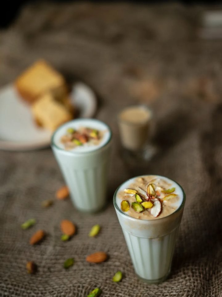 Glasses of sweet and salted lassi garnished with pistachios, malai, roasted cumin and mint