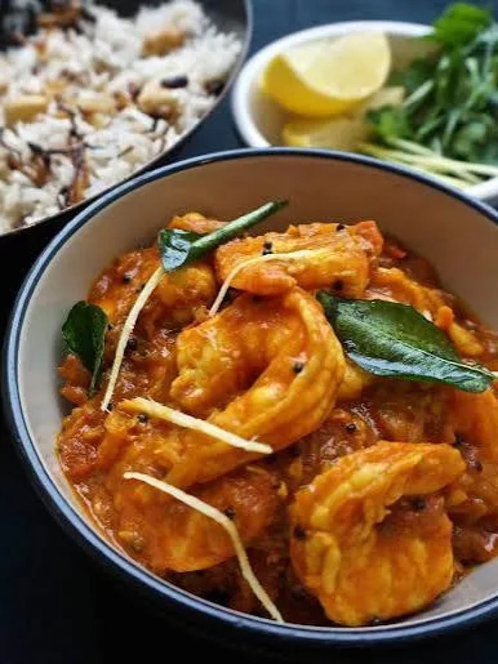A pan of Malabar prawn curry in a rich orange coconut sauce with curry leaves, green chillies and coriander, served beside white rice.