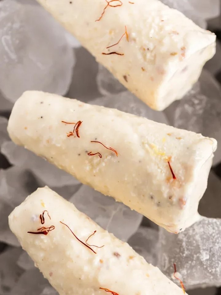Sliced malai kulfi topped with pistachios and saffron on a copper plate
