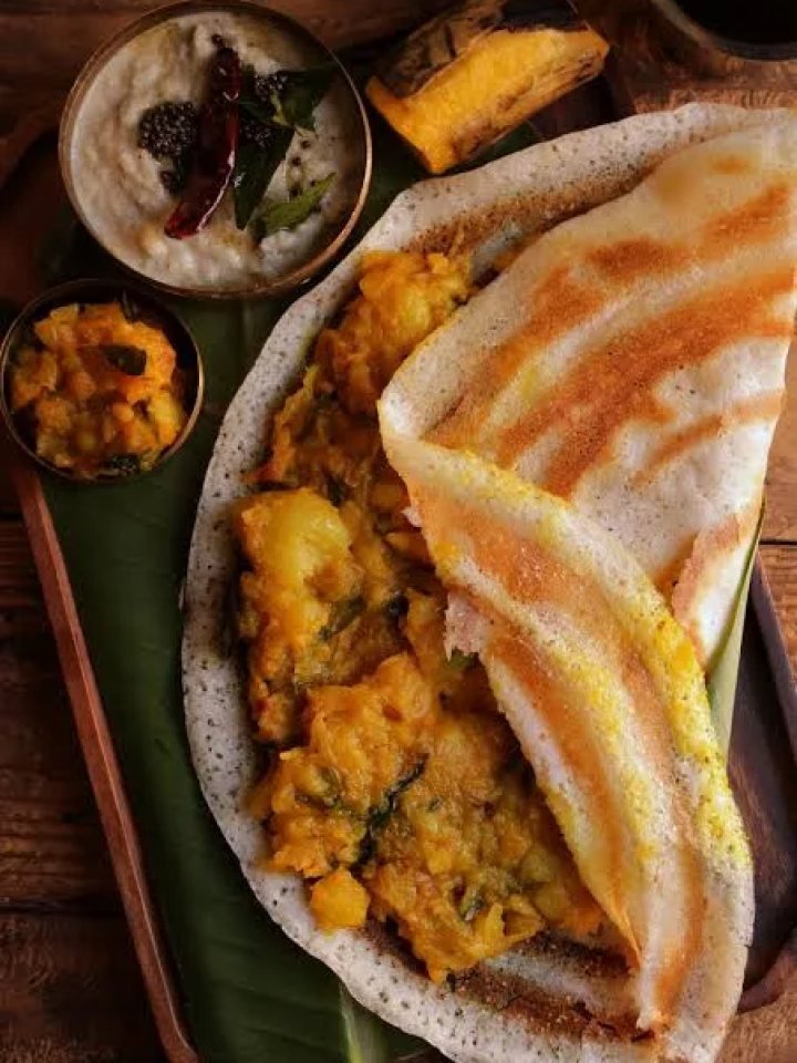 A crisp golden masala dosa filled with spiced potato, served with coconut chutney and sambar on a steel plate