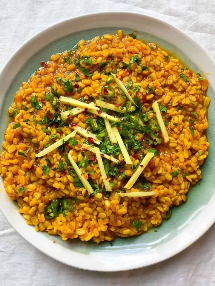 A brass bowl of creamy mash ki daal topped with garlic ghee tarka, red chillies and fresh coriander, served with roti and lemon wedges