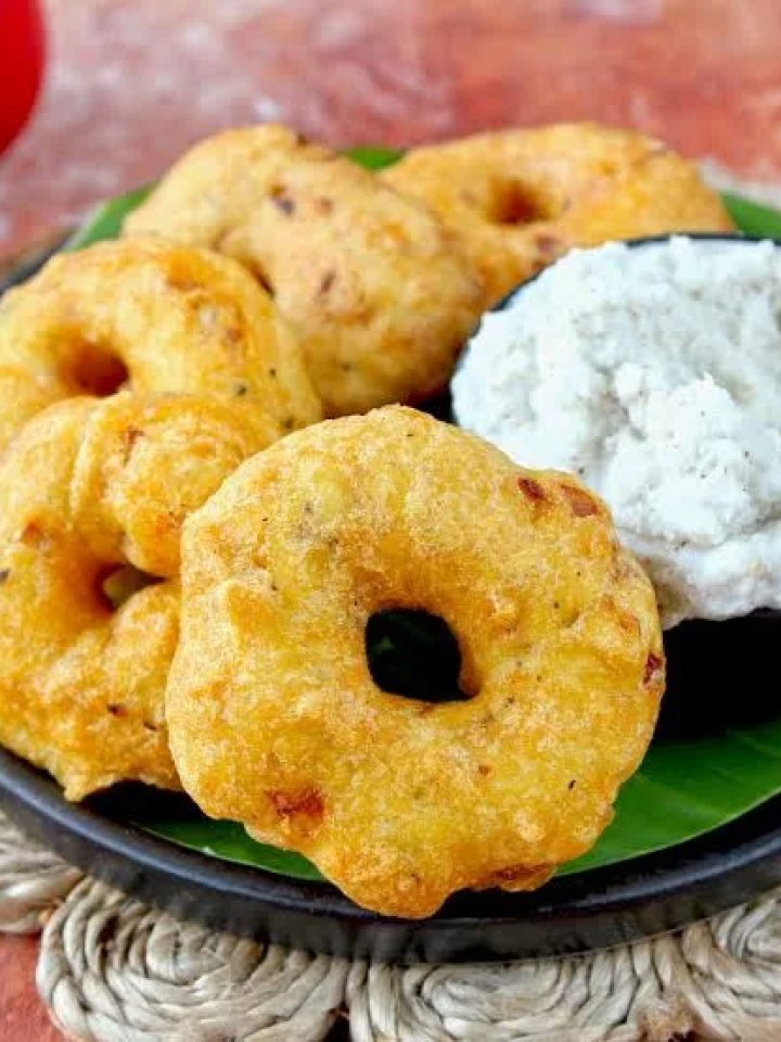 Golden medu vada doughnut-shaped fritters on a plate with coconut chutney and sambar, one broken open to show a soft centre