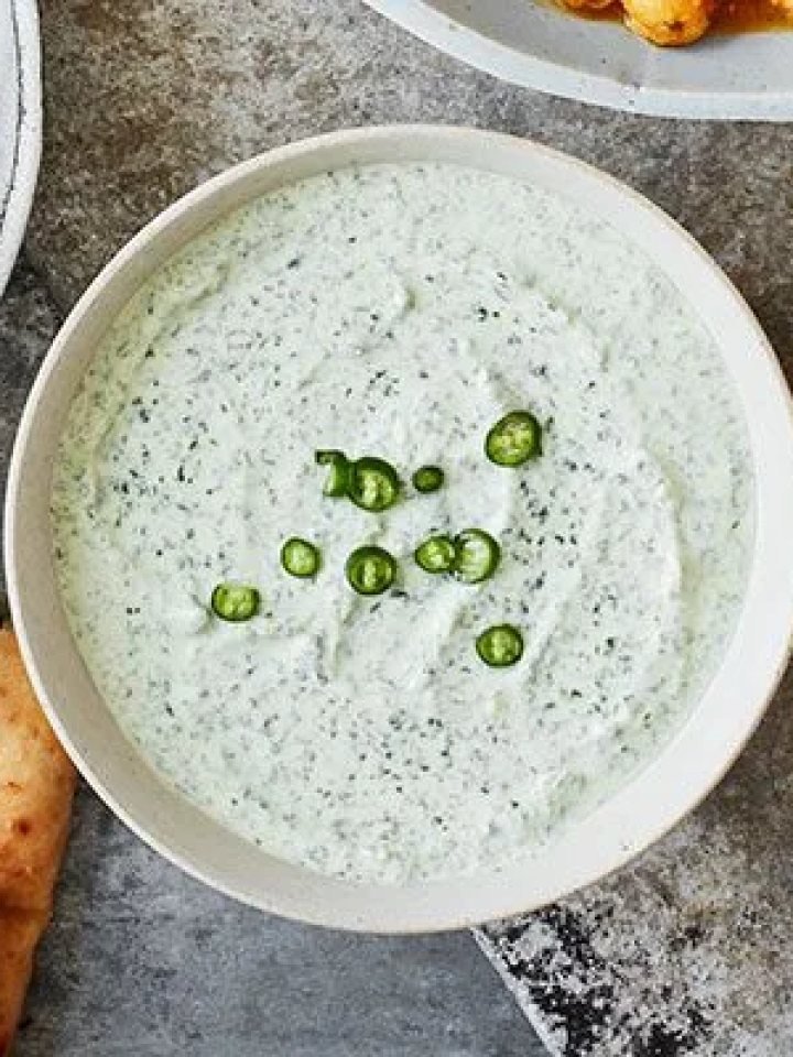 Bowl of creamy pale green mint raita topped with roasted cumin, chilli powder and fresh mint leaves