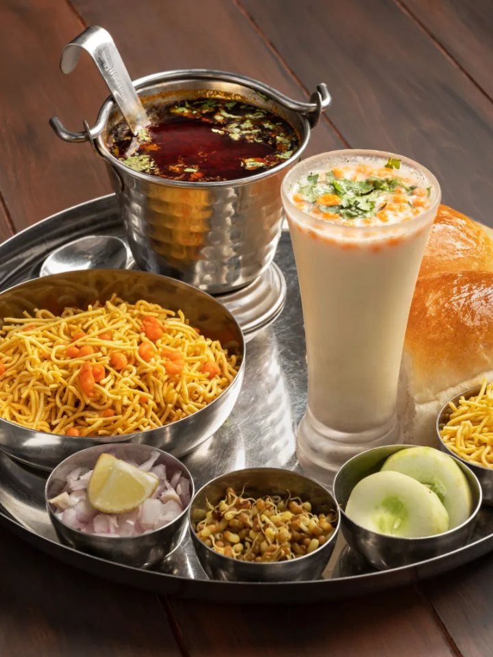 Bowl of misal with sprouted beans in red spicy gravy, topped with farsan, onion and coriander, served with buttered pav