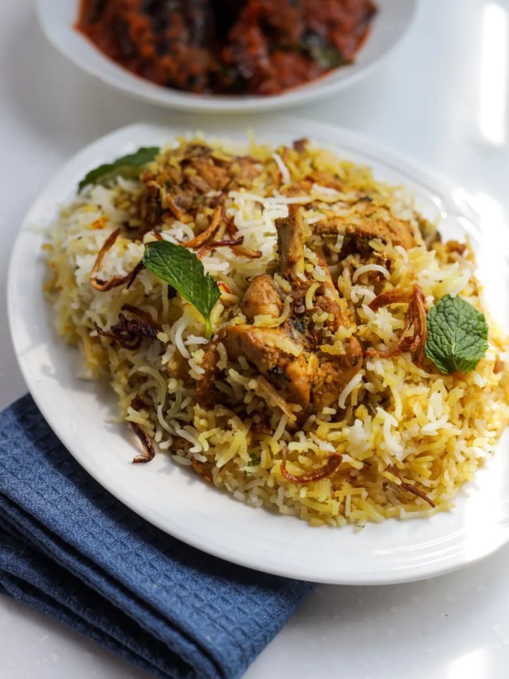A pot of mutton biryani with saffron rice, tender mutton pieces, fried onions and fresh herbs