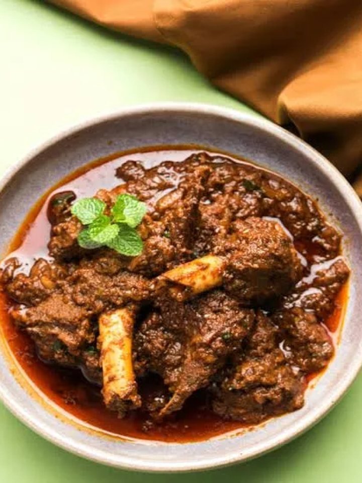 A copper pot of mutton korma with thick golden-brown gravy, garnished with ginger and coriander, served with naan