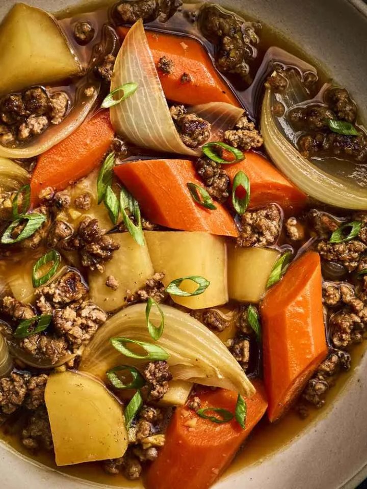 Bowl of Japanese nikujaga beef and potato stew with carrots, onion and green peas