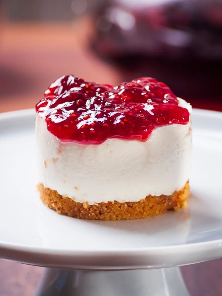 Slice of no-bake cheesecake with a biscuit base and fresh strawberry topping on a white plate