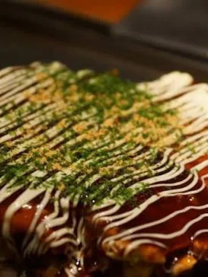 Okonomiyaki cabbage pancake topped with sauce, mayonnaise and nori, with one wedge cut out