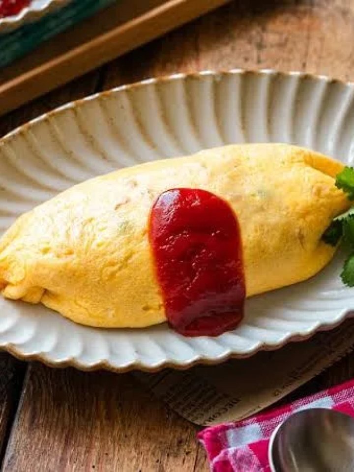 Soft yellow omelette over ketchup chicken rice, drizzled with ketchup and garnished with parsley